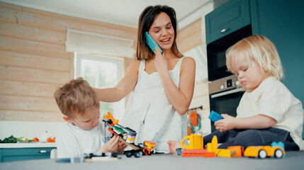 Young family mom and two kids boys are blonde. Play in the kitchen in a fun game children's designer in the kitchen. Happy summer time in a country house.