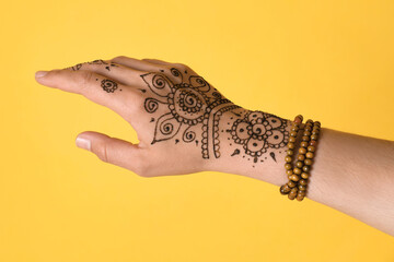 Wall Mural - Woman with beautiful henna tattoo on hand against yellow background, closeup. Traditional mehndi