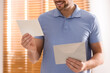 © New Africa - Man holding envelope with blank greeting card indoors. closeup