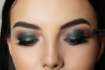 Applying dark eye shadow with brush onto woman's face, closeup. Beautiful evening makeup