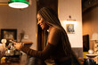 © Kike Arnaiz/Stocksy - Smiling black woman browsing smartphone in bar
