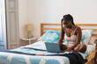 © Kike Arnaiz/Stocksy - Young black woman browsing laptop on bed