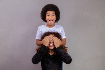 Wall Mural - African American boy holding his mother closed eyes. grey background. Mothers Day. Brazilian family.