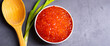 Red caviar in a wooden cup on a gray background with a spoon and green onions. A large pile of bright caviar. Fresh delicious caviar. A place for advertising, logo, label, layout, mockup.