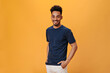 © Look! - Man in black t-shirt smiles sweetly on orange background. Portrait of guy in blue tee posing on isolated backdrop