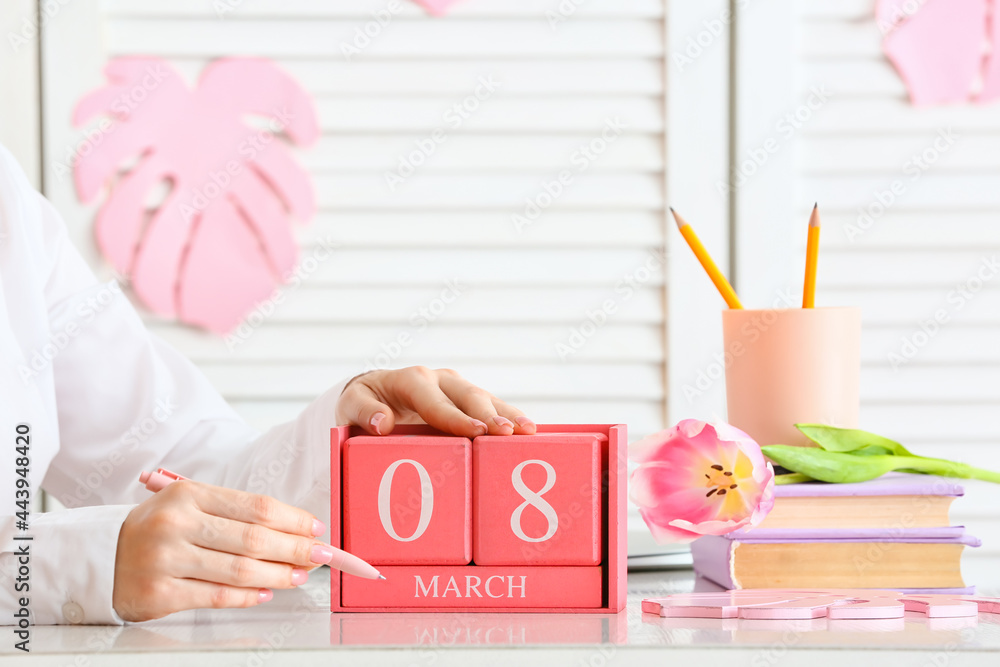 Woman holding cube calendar with date MARCH 8 on table in room