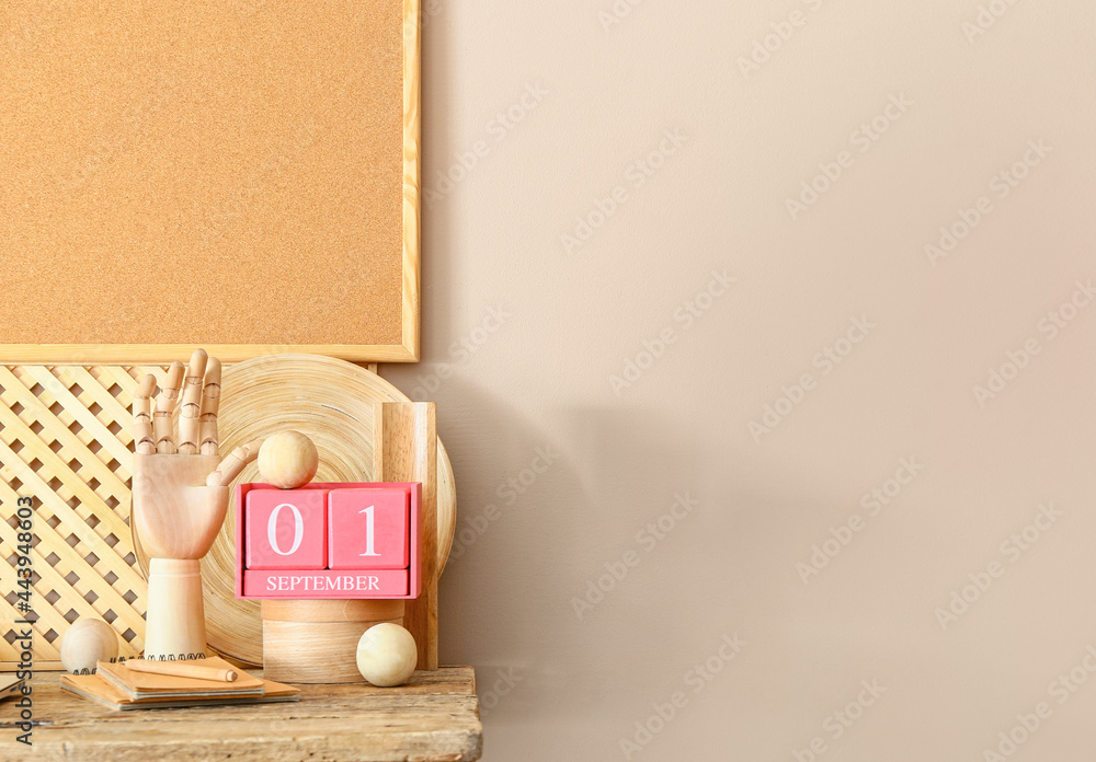 Cube calendar with date SEPTEMBER 1, notebooks and wooden hand on table in room
