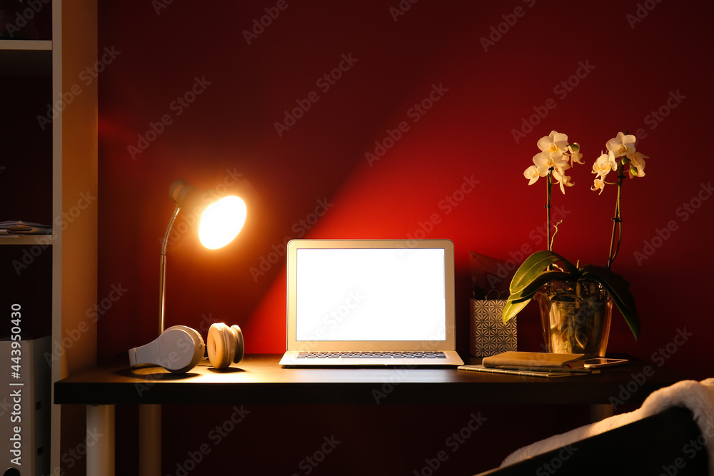 Modern workplace with laptop and glowing lamp near color wall