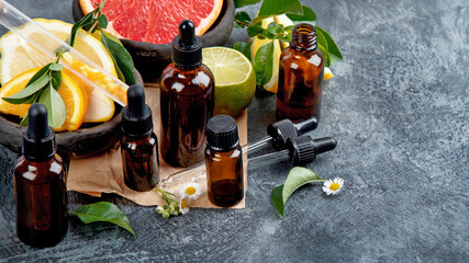 Bottles of essential aroma oils with citrus on dark gray background.