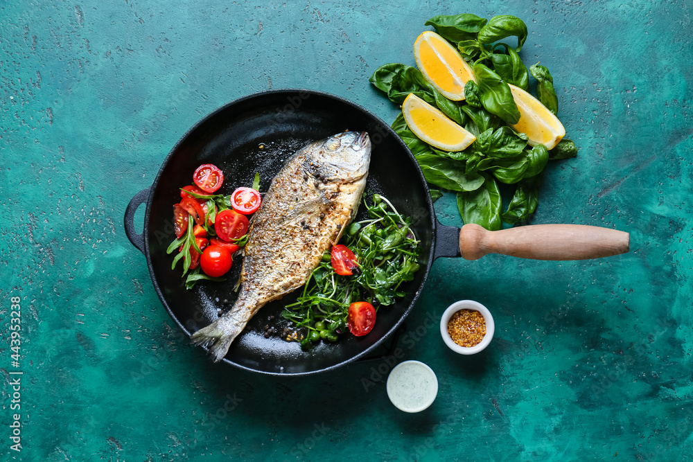 Frying pan with dorado and vegetables on color background