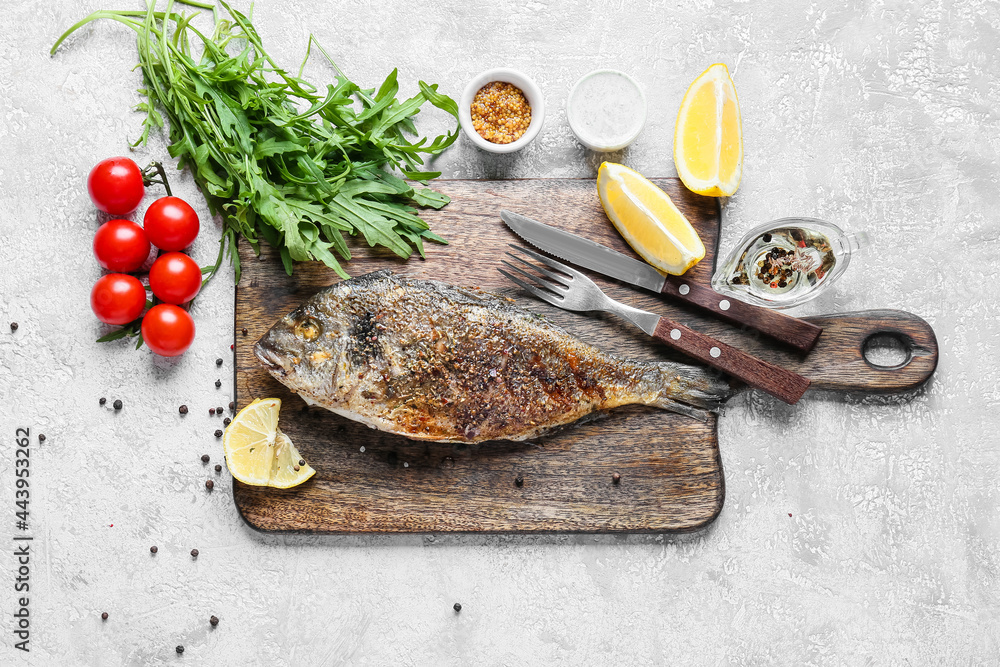 Wooden board with fried dorado on light background