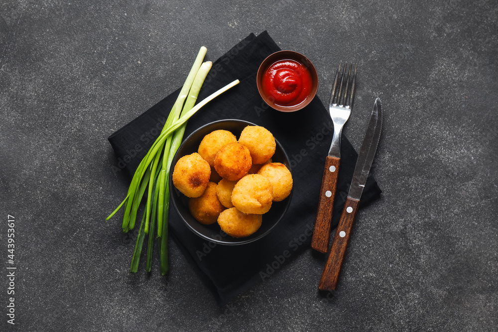 Bowl with fried potato balls and tomato sauce on dark background