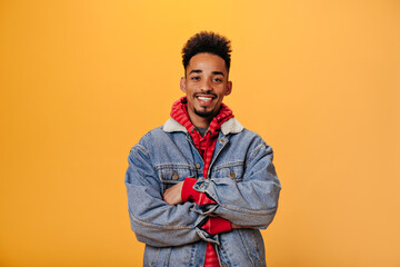 Young guy in denim jacket is smiling on orange background. Man in red hoodie looking into camera. Portraitof positive teen on isolated