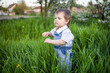 © YouraPechkin - Cute boy in fashionable clothes with blue eyes plays and jumps in the tall grass in a large green blooming garden