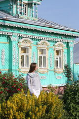 Wall Mural - Russian tourist woman in Suzdal town, Russia. Summer garden with flowers. Traditional national wooden house with carved frames, ornamental windows. Suzdal landmark. Wooden architecture. Russian style