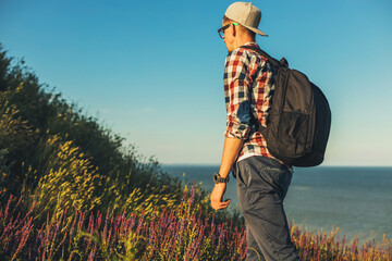 Wall Mural - Young man, goes on a hike, with a backpack, Smiling man goes up the mountain, travel Lifestyle, summer vacation outdoors