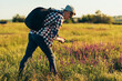 © Shopping King Louie - Young man in a cap with a backpack, traveling and walking in nature, a tourist collects flowers on the field, the concept of tourism