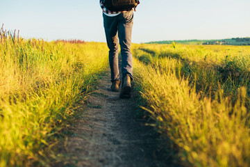 Active tourist, a man with a briefcase in nature, a hipster in a cap is walking along a path on a green hill, healthy lifestyle