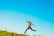 © Shopping King Louie - Happy young tourist with a backpack, happy jumping man with hands up against a blue sky background, climbs to the top of a hill or mountain