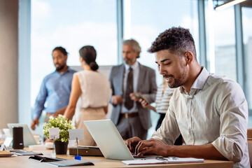 Wall Mural - Successful leaders build successful teams. Businessman Using Laptop At Desk In Busy Office. Serious dark-skinned young office manager works with different reports and table laptop 