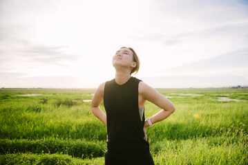 Young happy woman in black dress in green field, evening light.