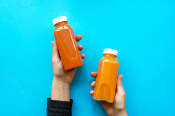 A woman is holding an orange and carrot detox juices or smoothies on a blue background. The concept of diets, detox, body care.