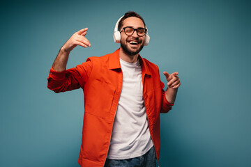 Wall Mural - Positive man in orange jacket smiles and enjoys music in headphones