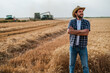 © djoronimo - Farmer is standing in front of his wheat field while harvesting is taking place.
