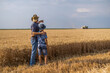 © djoronimo - Farmers are standing in their wheat field while the harvesting is taking place. Father is teaching his son about agriculture.