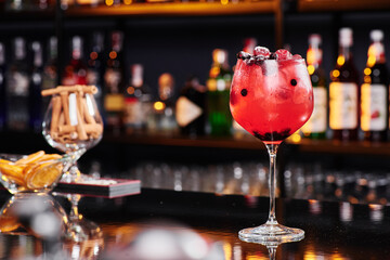 Red fruit cocktail in an elegant glass against the background of a bar in a nightclub. Space for text. High quality photo