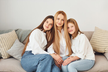 Sitting on the sofa. Young mother with her two daughters at home at daytime