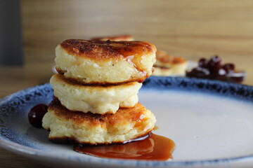 Canvas Print - Three pancake cheesecakes lie stack of slides on top of each other on plate table with cherry cherry . View from the side. Breakfast is Russian Ukrainian. Dishes cottage cheese. Place with copyspace