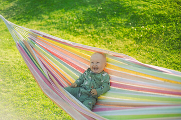 portrait of adorable baby boy     in the park with green lawn is smiling next to the hammock  . Happy childhood