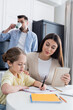 © LIGHTFIELD STUDIOS - blurred man drinking coffee near daughter doing homework together with mom