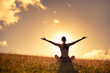 © kieferpix - Young happy woman sitting in a grass field lifting her arms up to the sky feeling joy and freedom.