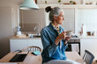 © BONNINSTUDIO/Stocksy - Glad mature woman enjoying hot drink in kitchen