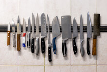 Many Different Knives Are Attached To A Magnetic Knife Holder On The Wall.