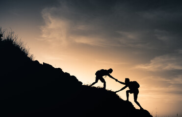 Help and assistance concept. Silhouettes of two people climbing on mountain and helping.