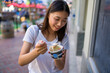 Happy Young Asian Woman Wearing Distressed Jeans and T-Shirt Eating an Ice Cream Sandwich in a Downtown Urban Area