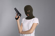 Woman wearing knitted balaclava with gun on grey background