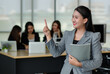 © Bangkok Click Studio - Portrait of young attractive Asian female office worker in formal business suits  smiling at camera in office with blurry colleagues sitting in office as background