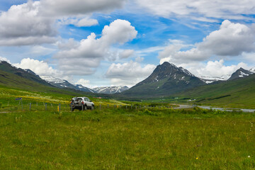 Wall Mural - Landscape view of mountains and green grass in fresh and bright summer, white car running on Icelandic countryside road. On a holiday trip, blue sky and beautiful clouds.