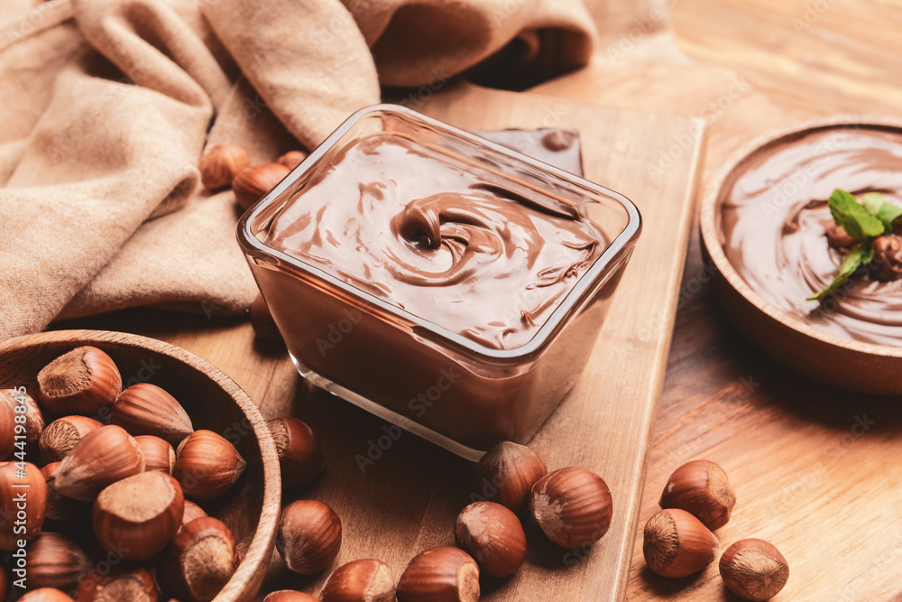 Bowl with tasty chocolate paste and hazelnuts on wooden background