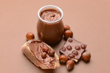 Wall Mural - Jar and bread with tasty chocolate paste and hazelnuts on color background