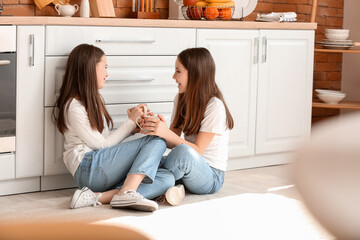 Poster - Cute twin girls with cups sitting on kitchen floor