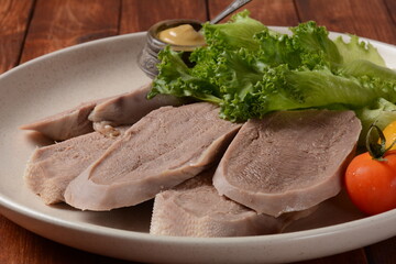 Wall Mural - Sliced Beef Tongue Slices on a platter with lettuce leaves, cherry tomatoes and Dijon mustard on a wooden background