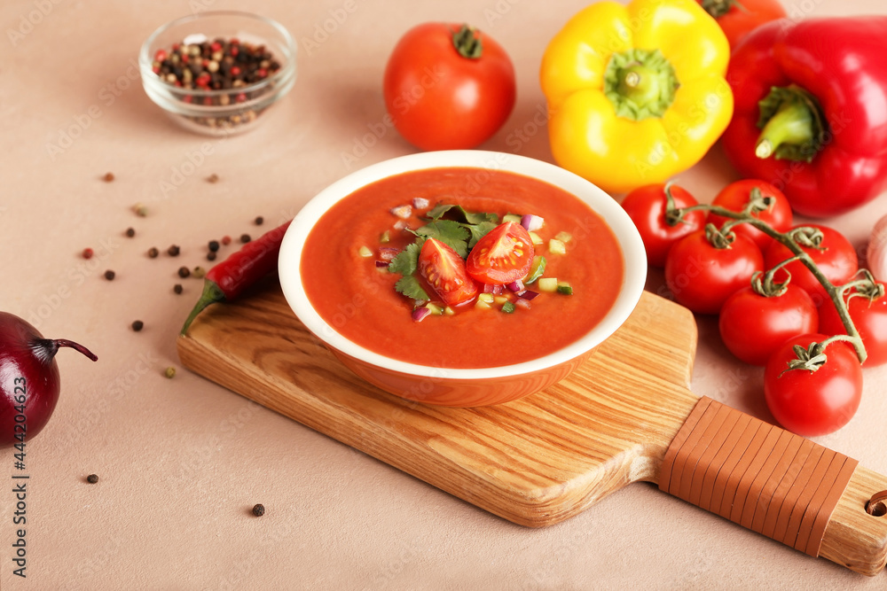 Bowl with tasty gazpacho and vegetables on color background