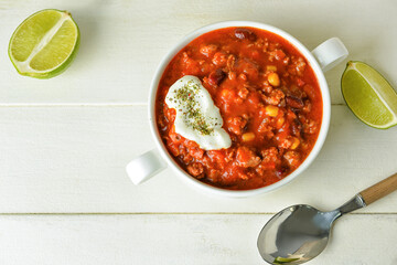 Pot with delicious chili con carne on light wooden background