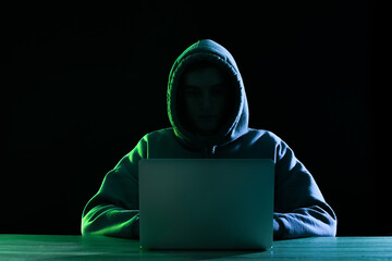 Silhouette of hacker with laptop at table on dark background