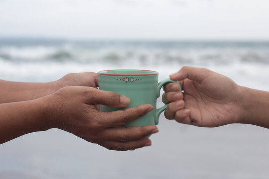 Wall Mural -  - Hands of two people holding a cup of coffee or tea on beach background. Take and give or giving and receive concepts. Kindness concept.